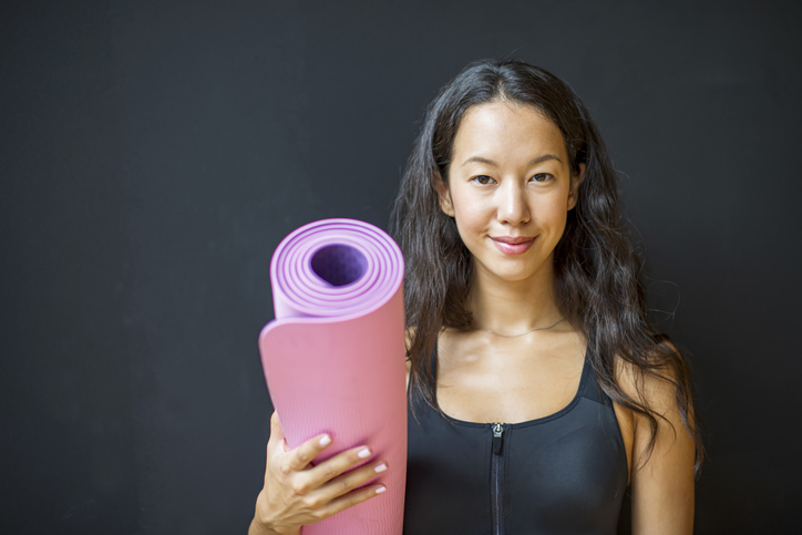 Cheerful woman holding exercise mat in fitness studio.